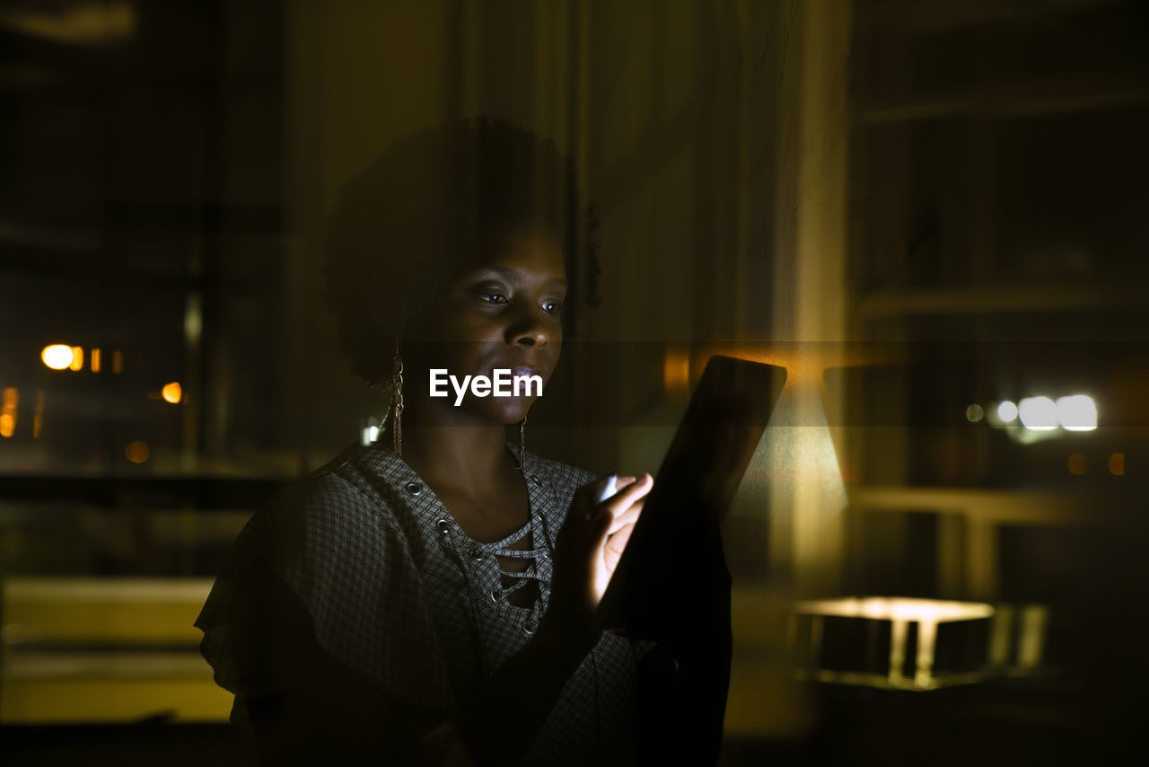 Businesswoman using tablet computer in dark office seen through glass