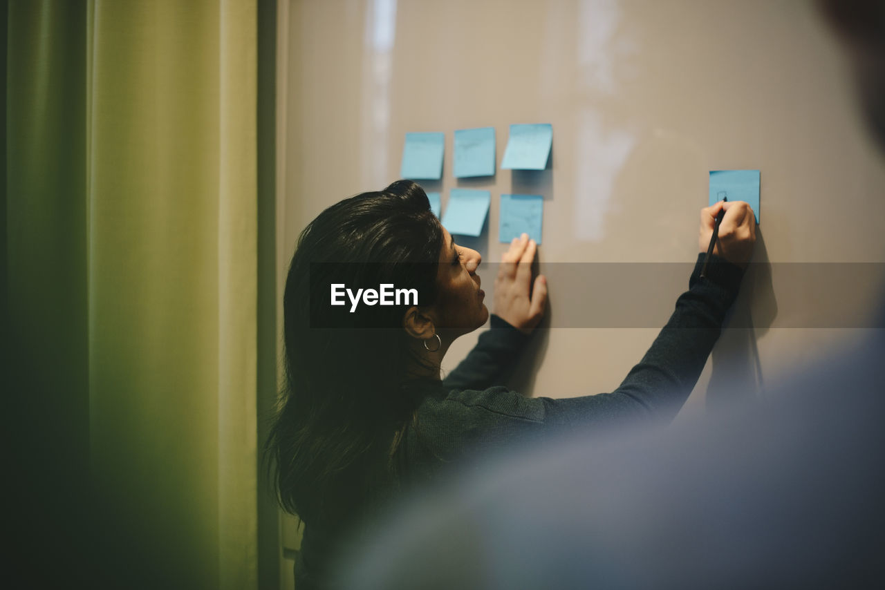 Rear view of businesswoman analyzing adhesive notes stuck on whiteboard in office