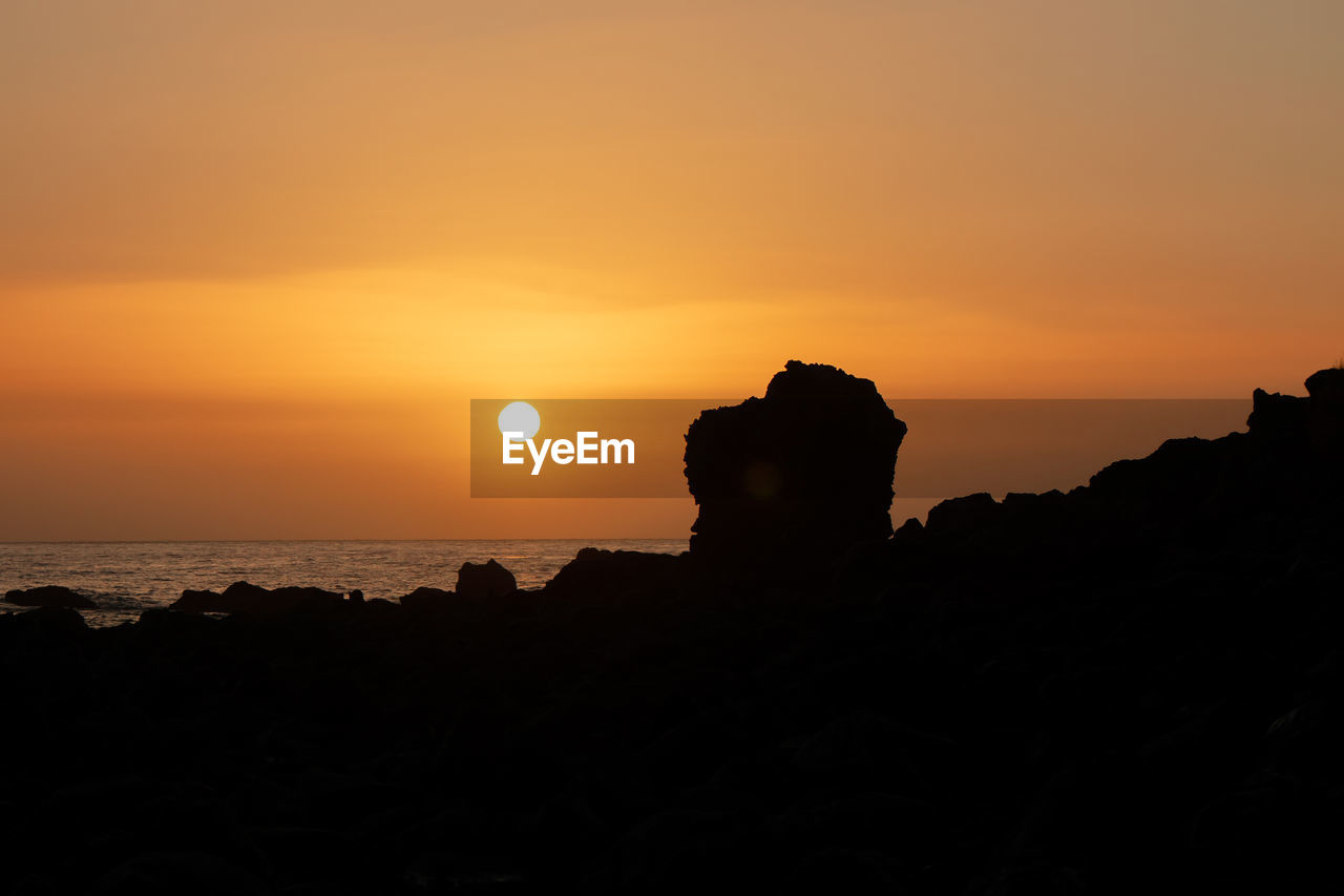 SILHOUETTE ROCKS ON SEA AGAINST ORANGE SKY