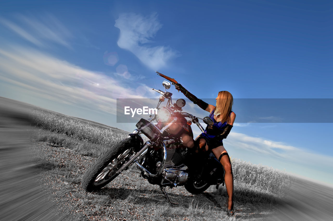 Woman with gun sitting on motorcycle against sky