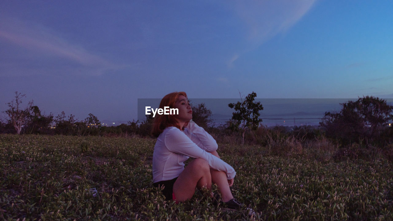 Woman sitting on field against sky