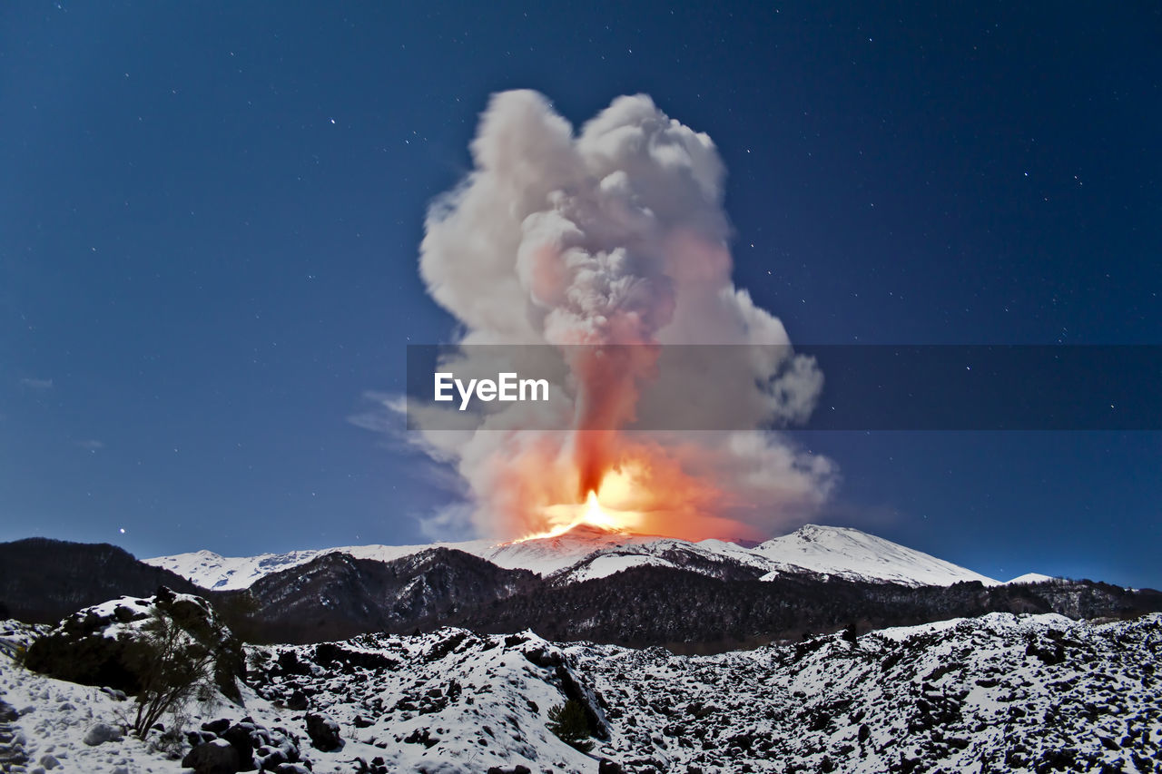 Volcano exploding against sky during sunset