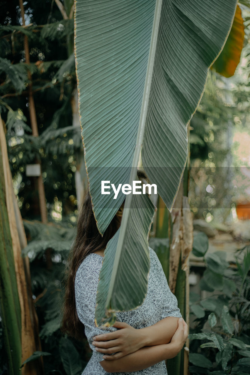 A young woman standing behind a plant leaf