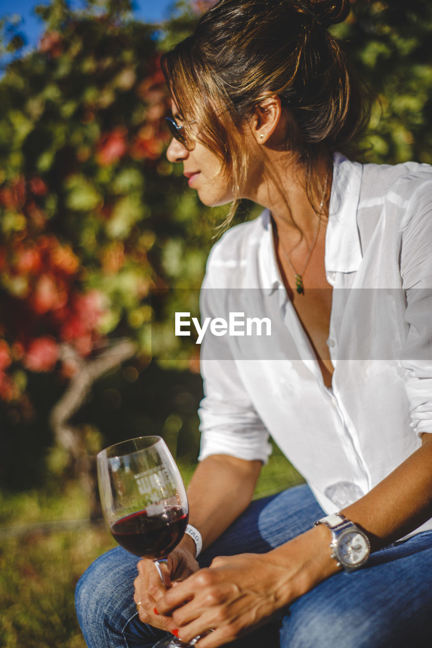 Woman in sunglasses having red wine against plants