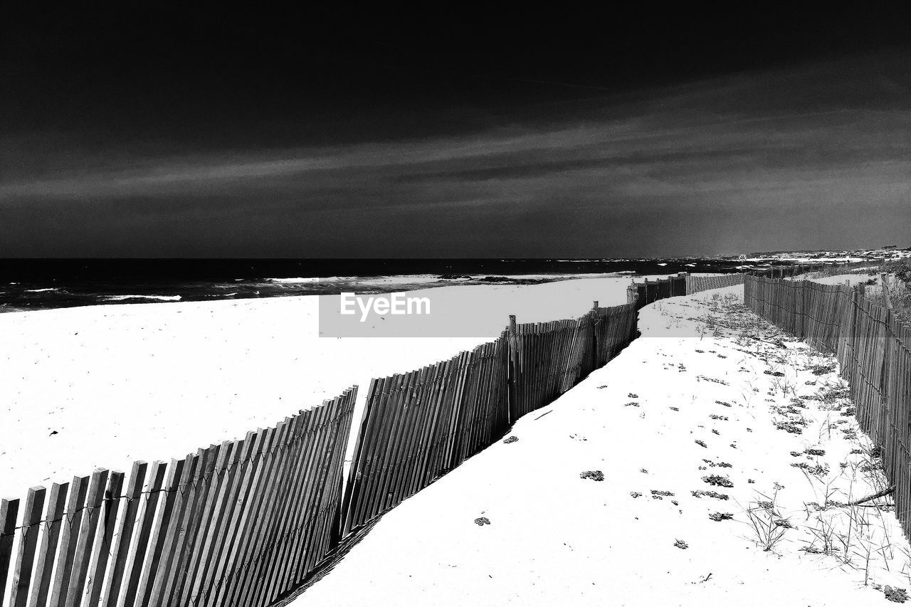 Fence at sandy beach against sky