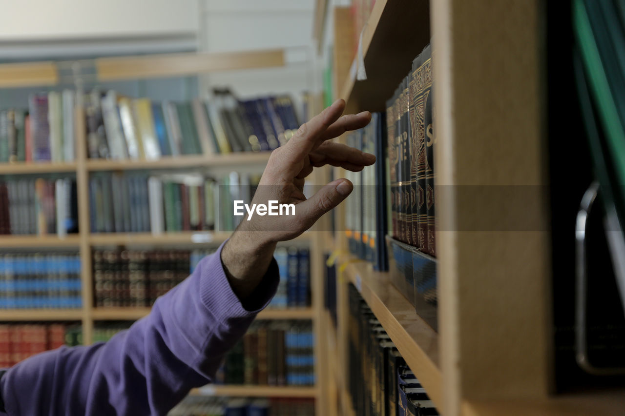 Cropped hand of man touching book in shelf