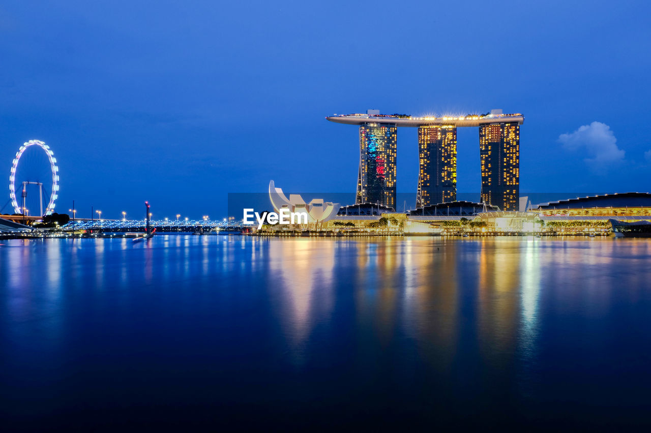 Marina bay sands by bay of water against sky in city at dusk