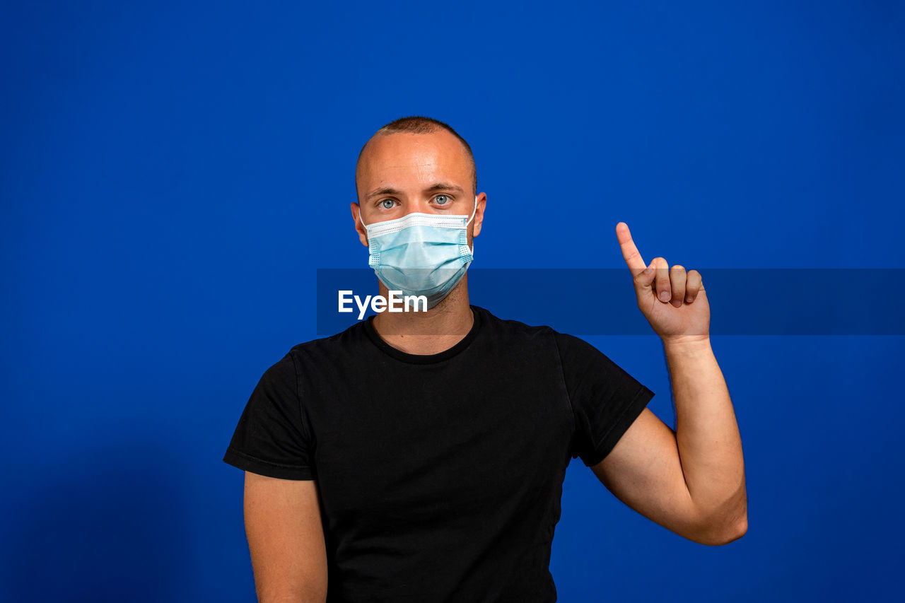 blue, one person, studio shot, adult, men, portrait, colored background, healthcare and medicine, looking at camera, blue background, front view, indoors, waist up, human face, arm, person, copy space, clothing, finger, protective mask - workwear, gesturing, communication, standing