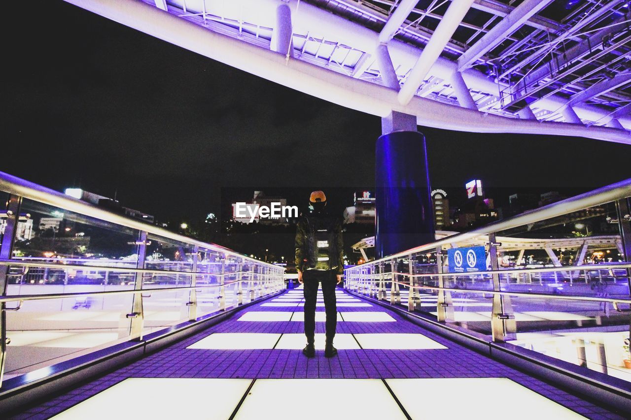 WOMAN WALKING ON ILLUMINATED BRIDGE AT NIGHT