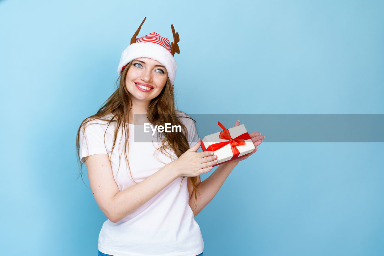 one person, women, smiling, studio shot, colored background, happiness, portrait, blue, young adult, emotion, adult, looking at camera, blue background, long hair, indoors, cheerful, fun, red, holding, copy space, clothing, hat, casual clothing, standing, hairstyle, female, celebration, flag, waist up, positive emotion, cute, holiday, blond hair, person, front view, lifestyles, fashion
