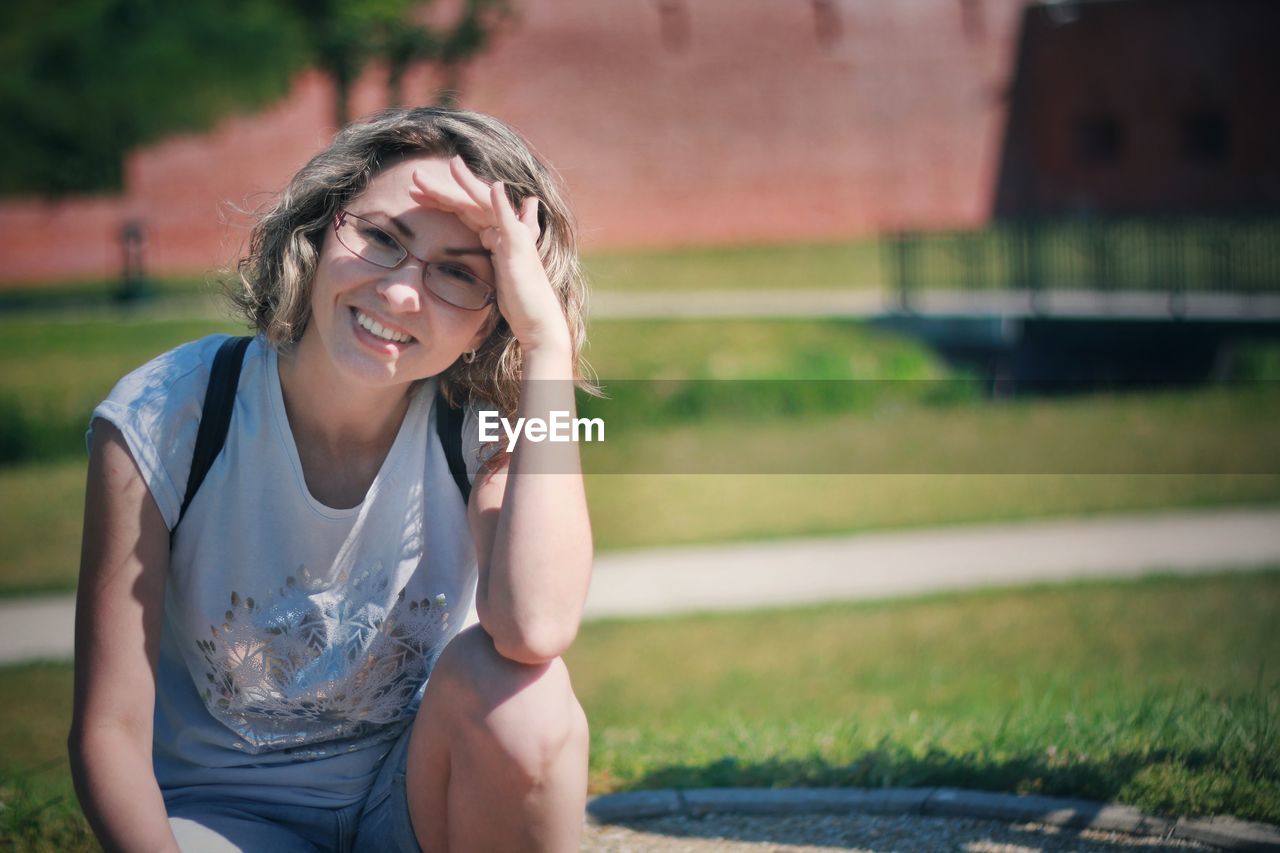 Portrait of smiling woman shielding eyes while sitting outdoors