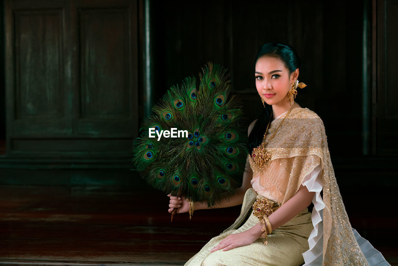 Portrait of young woman wearing traditional clothing and holding peacock feather