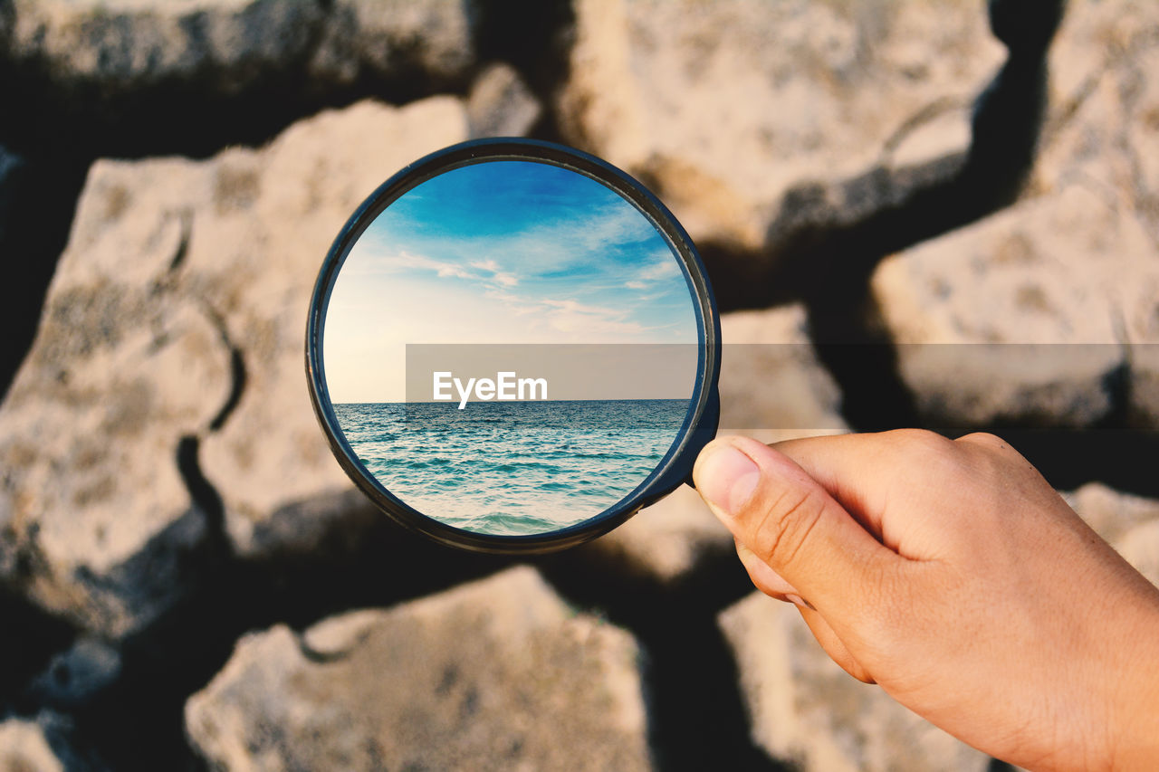 Digital composite image of woman holding magnifying glass with reflection of sea over barren land