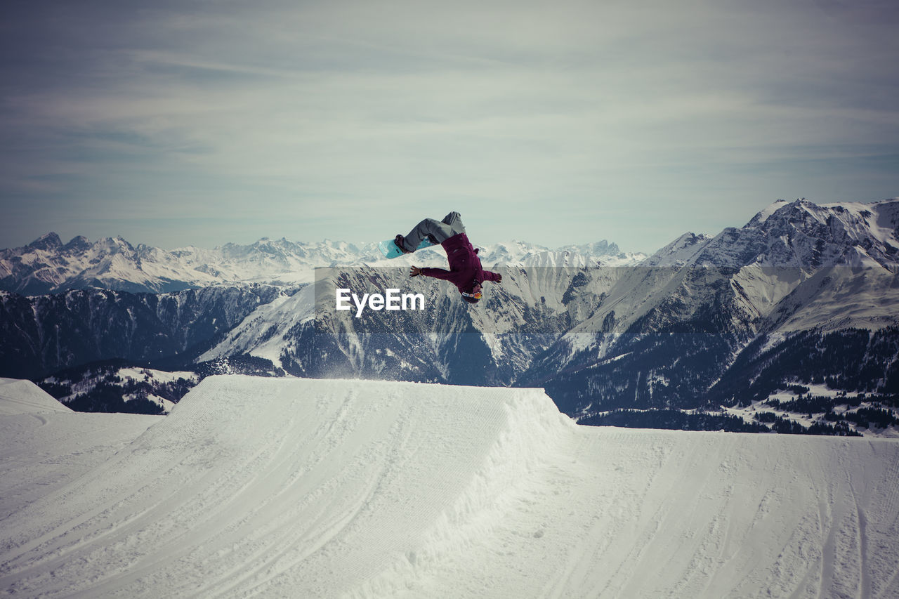 Snowboarder jumping against sky at mountain