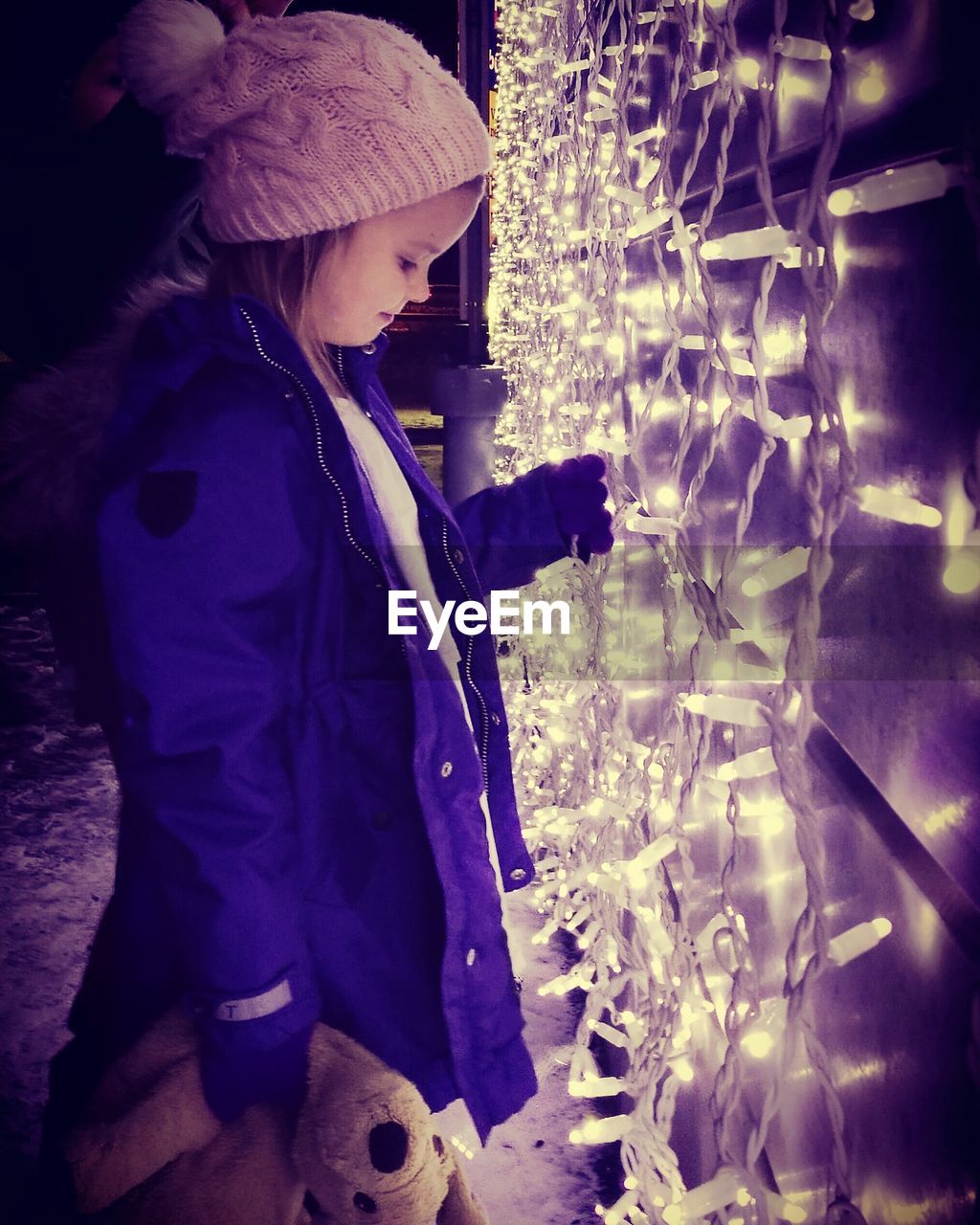 Side view of girl touching illuminated decoration during christmas at night
