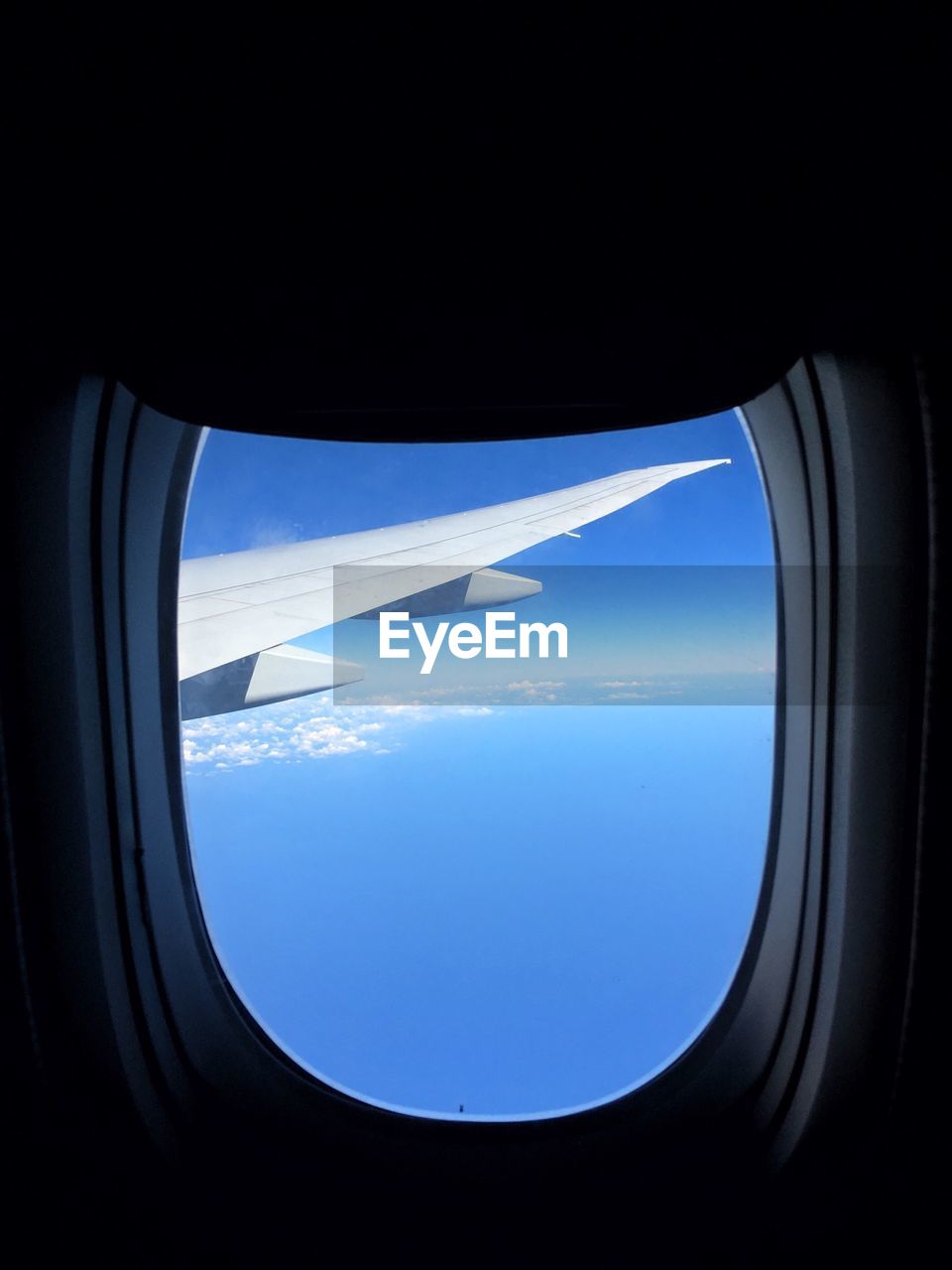 Cropped image of flying airplane seen through window glass