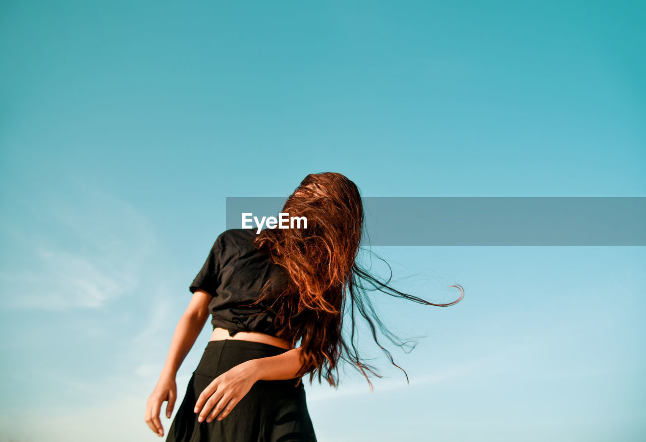 Low angle view of woman tossing hair against clear sky