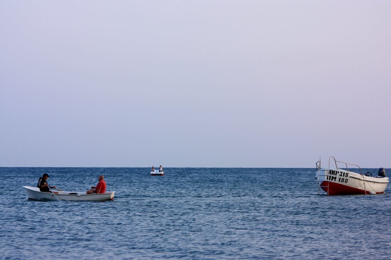 Men sailing in rowboat against clear sky