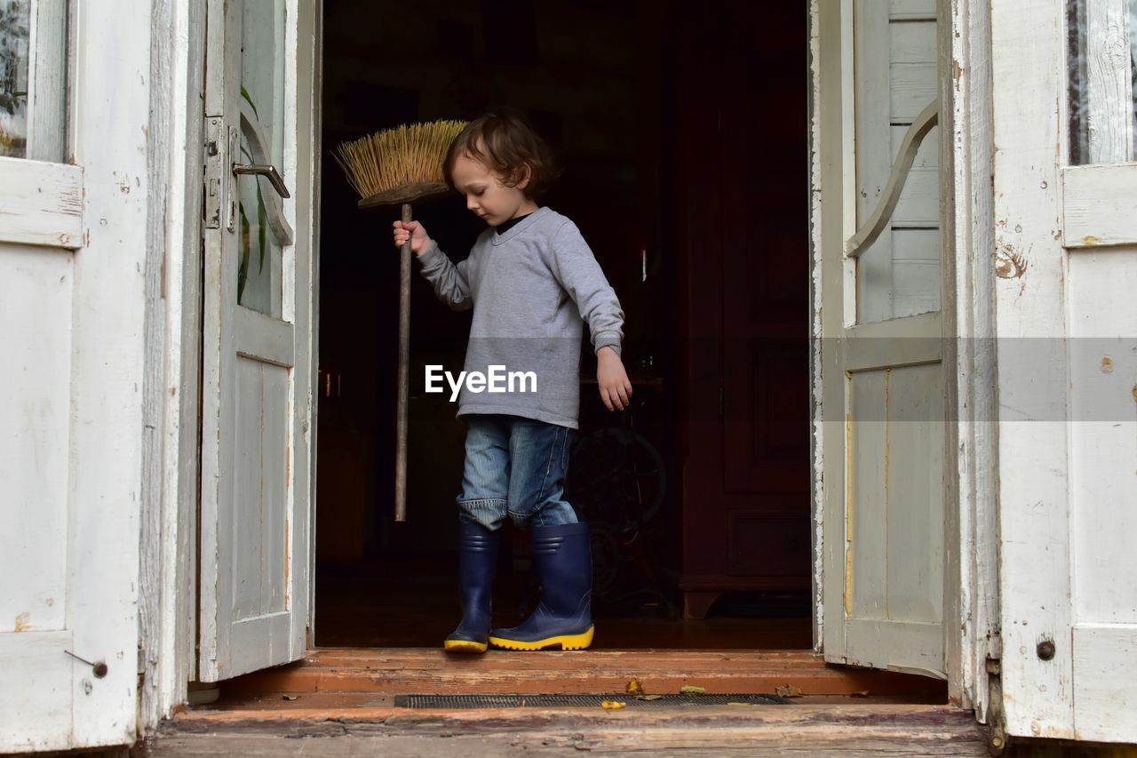 Full length of boy holding broom on doorway