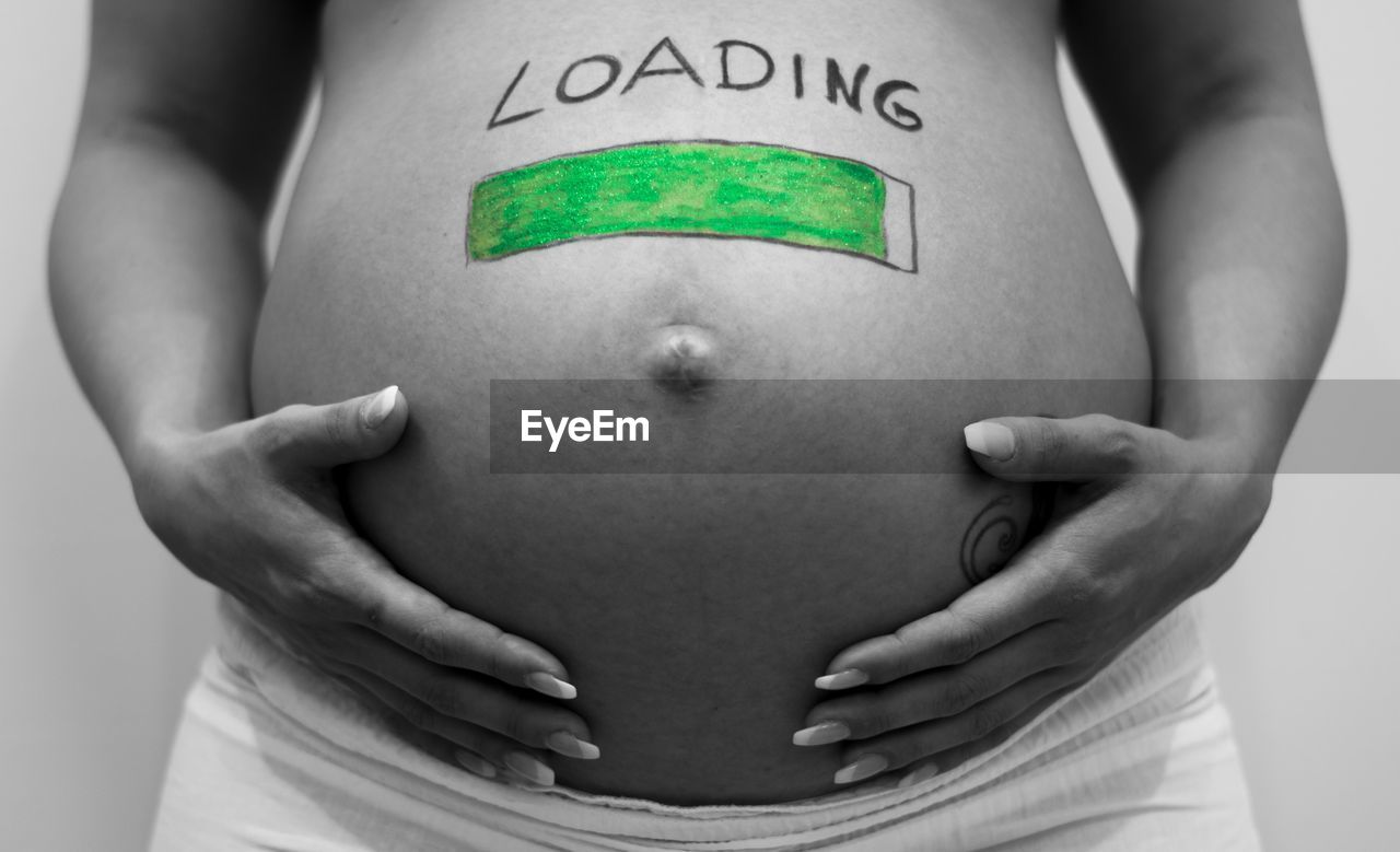 Midsection of pregnant woman with loading text and drawing on stomach against wall
