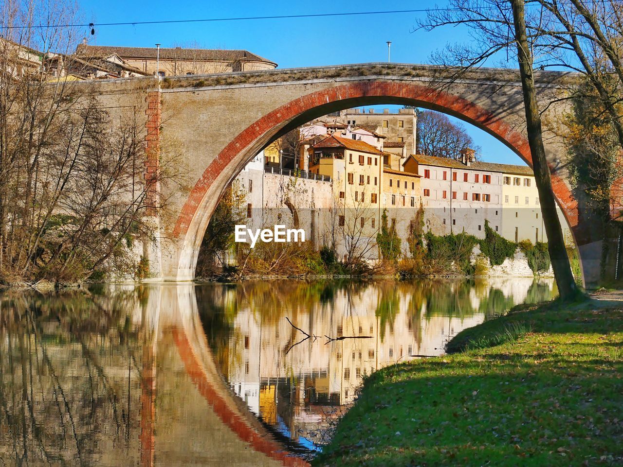 Arch bridge over lake by buildings against sky