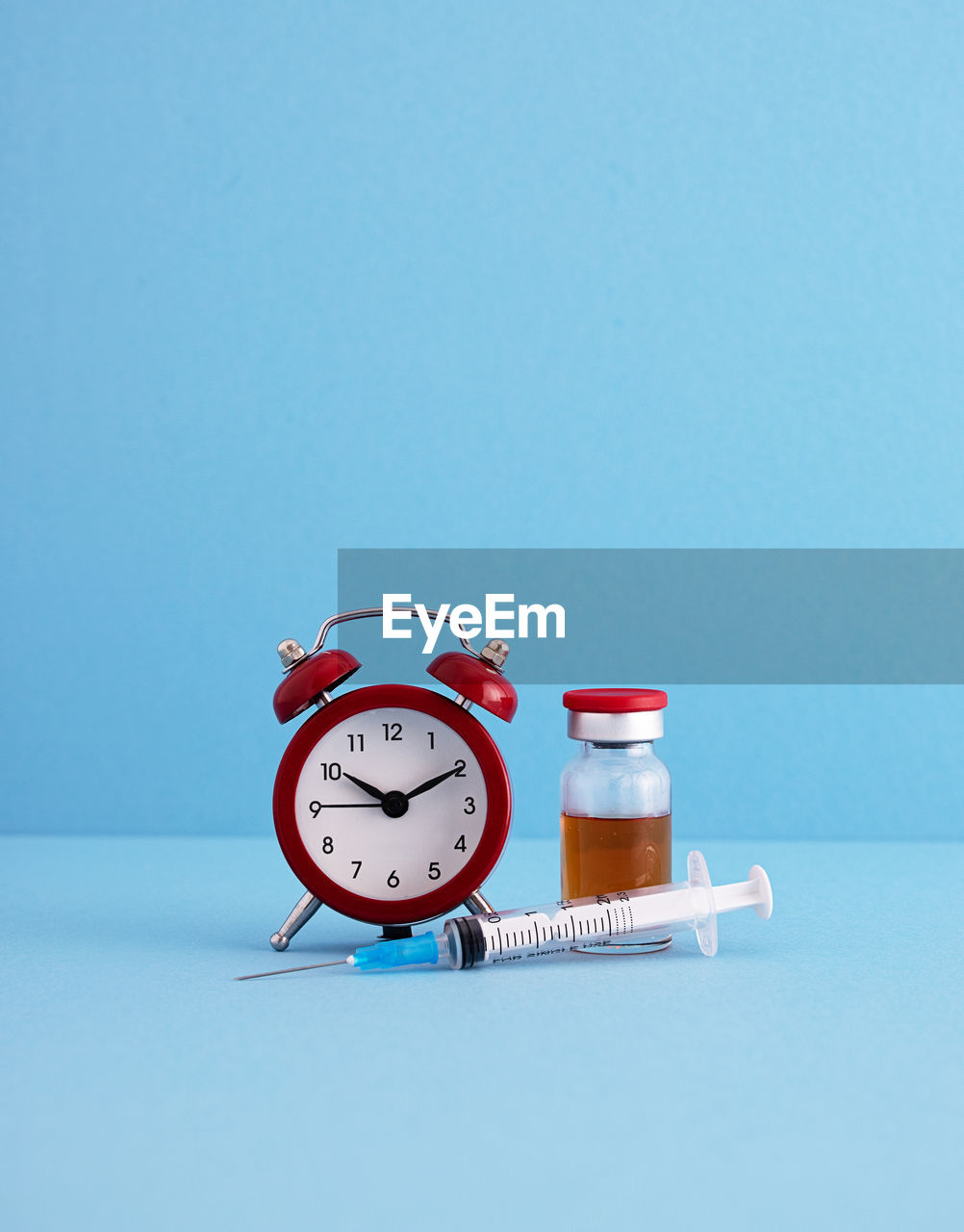 Close-up of coronavirus vaccine with alarm clock on blue background