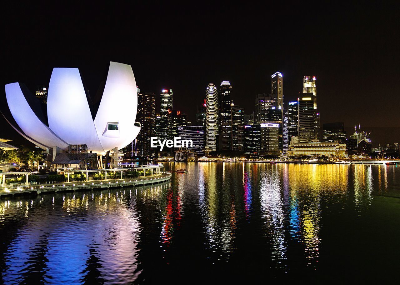 Illuminated city by river against sky at night