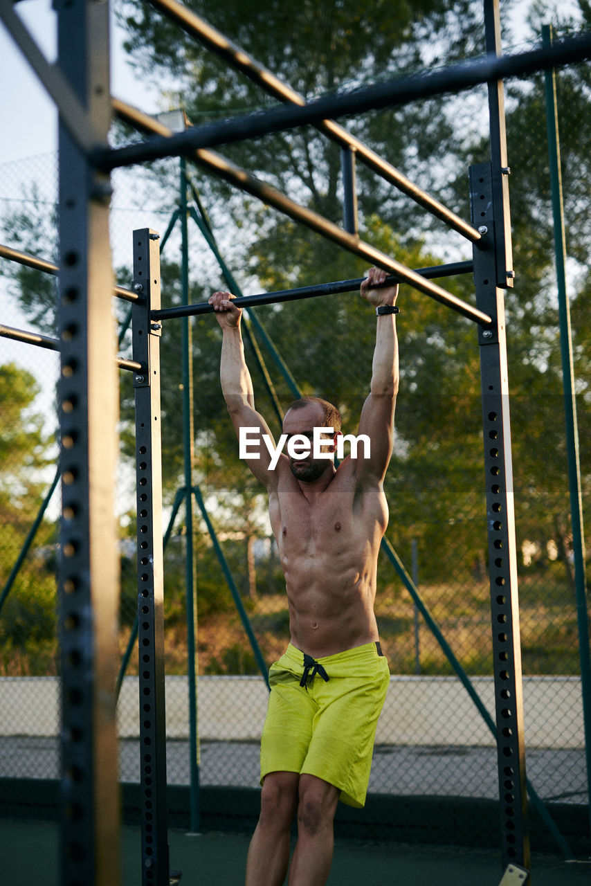 Shirtless fit young man working out in a cage at outdoors gym