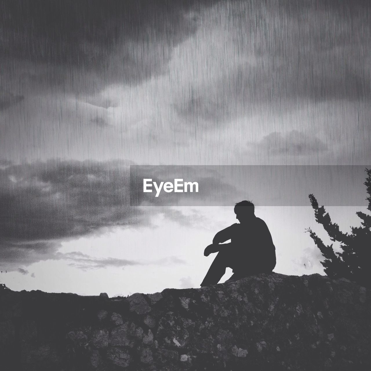 Silhouette man sitting on rock against sky