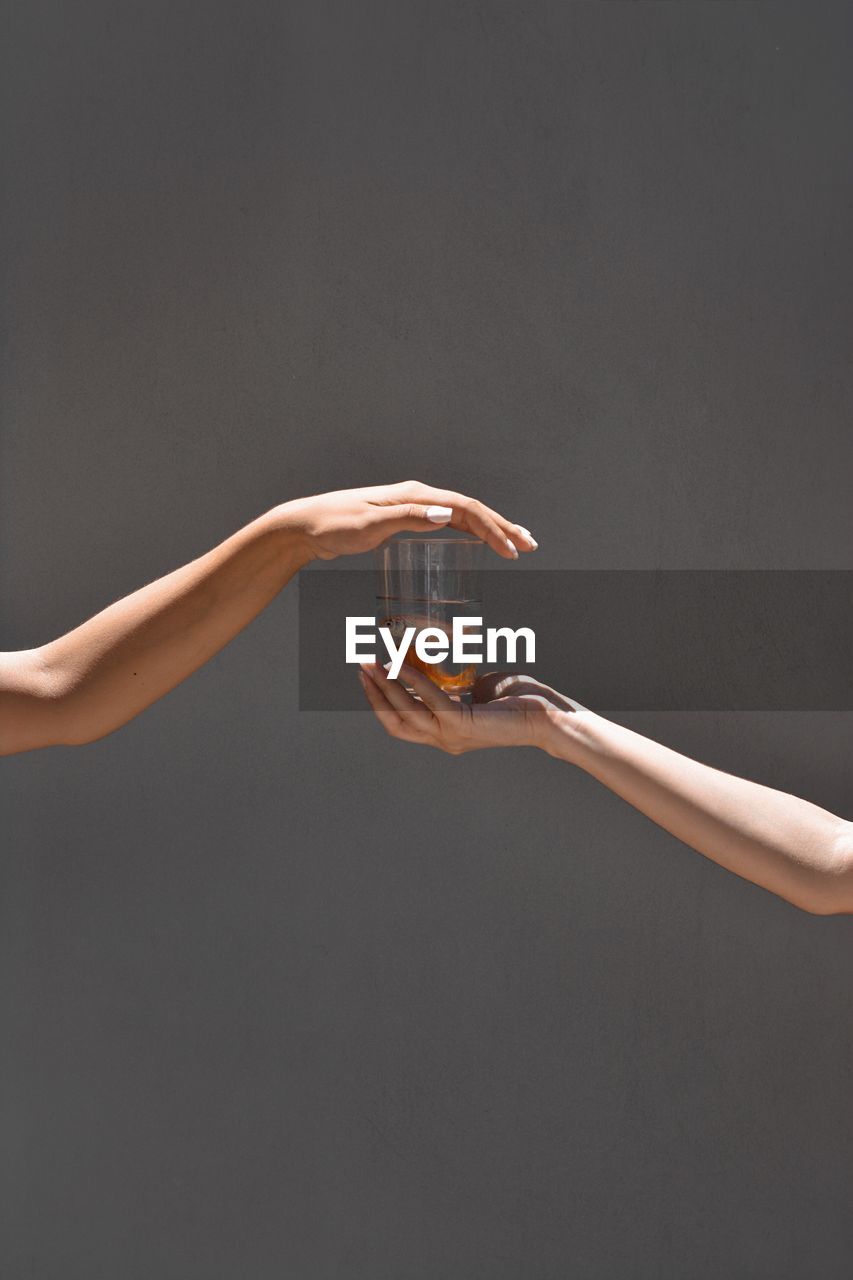 Cropped hands of people holding fish in drinking glass against gray background
