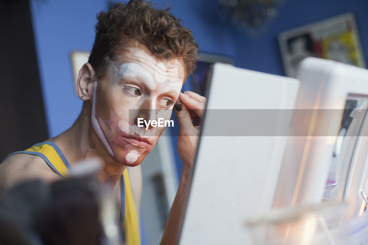 Young man putting on drag makeup
