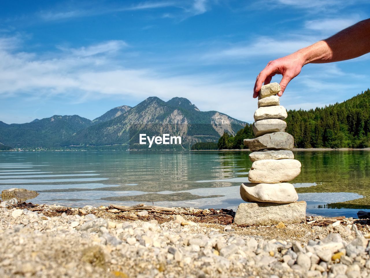 HUMAN HAND ON ROCK AGAINST LAKE
