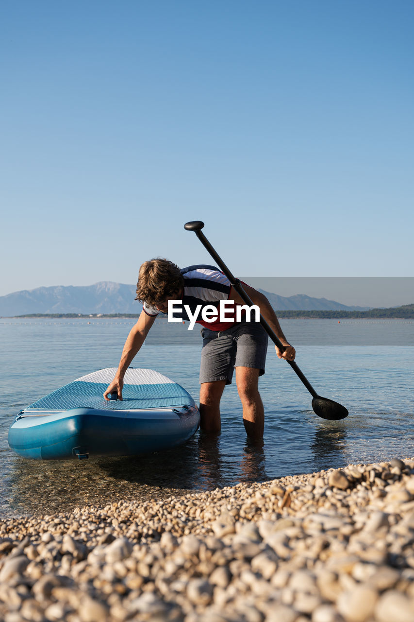 Man with paddleboard and oar standing in lake against clear sky