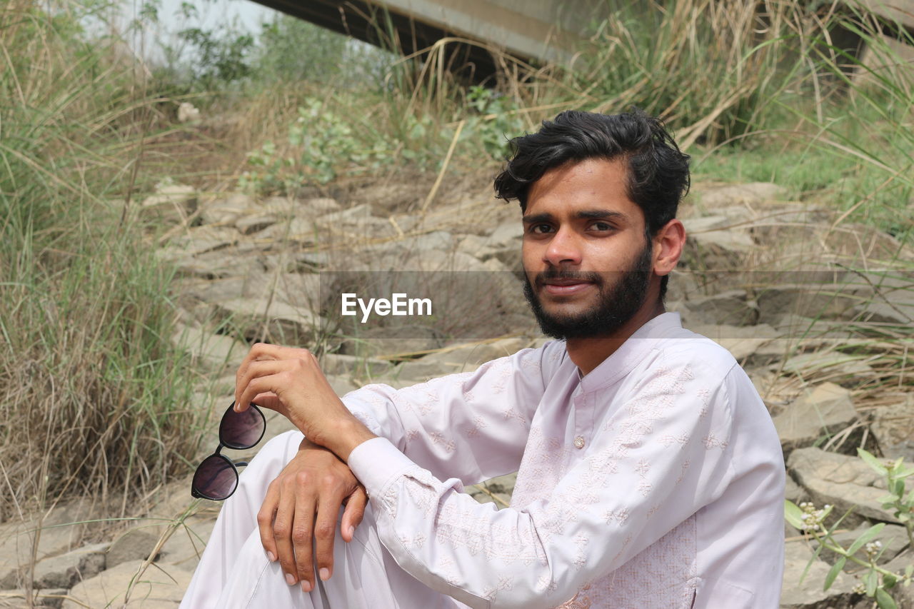 one person, men, adult, young adult, beard, plant, nature, facial hair, portrait, person, land, occupation, looking at camera, lifestyles, sitting, day, leisure activity, outdoors, traditional clothing, front view, casual clothing, clothing, holding, waist up, white, button down shirt
