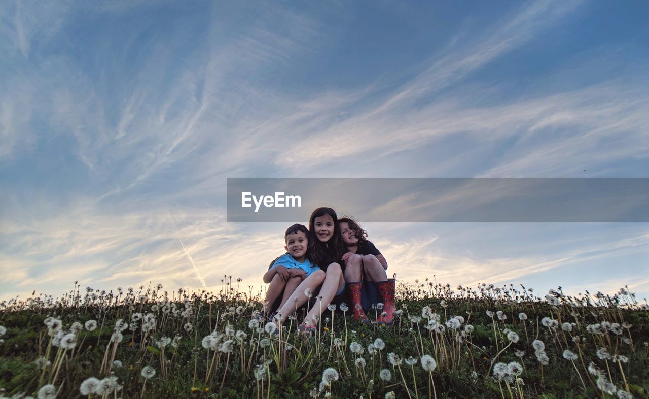 Low angle view of siblings sitting on grass against sky