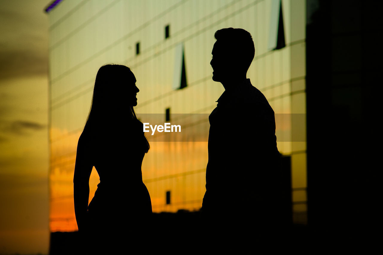 Silhouette couple standing against building during sunset