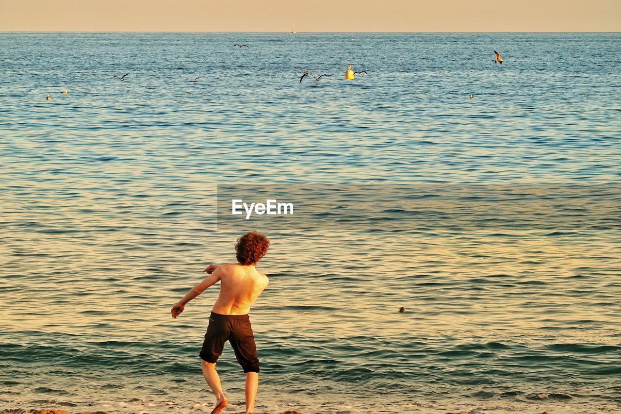 Shirtless teenage boy running towards sea at beach