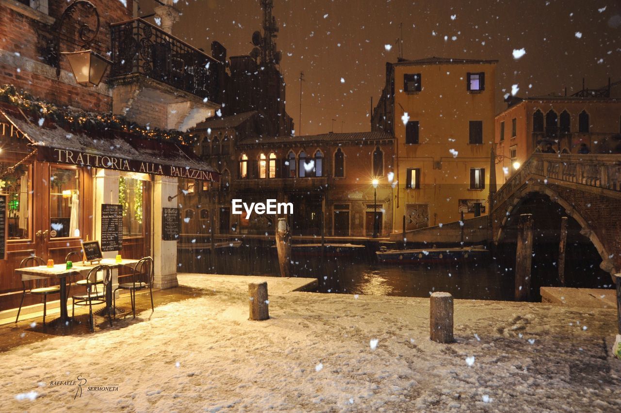 Illuminated buildings in city at night during snowfall