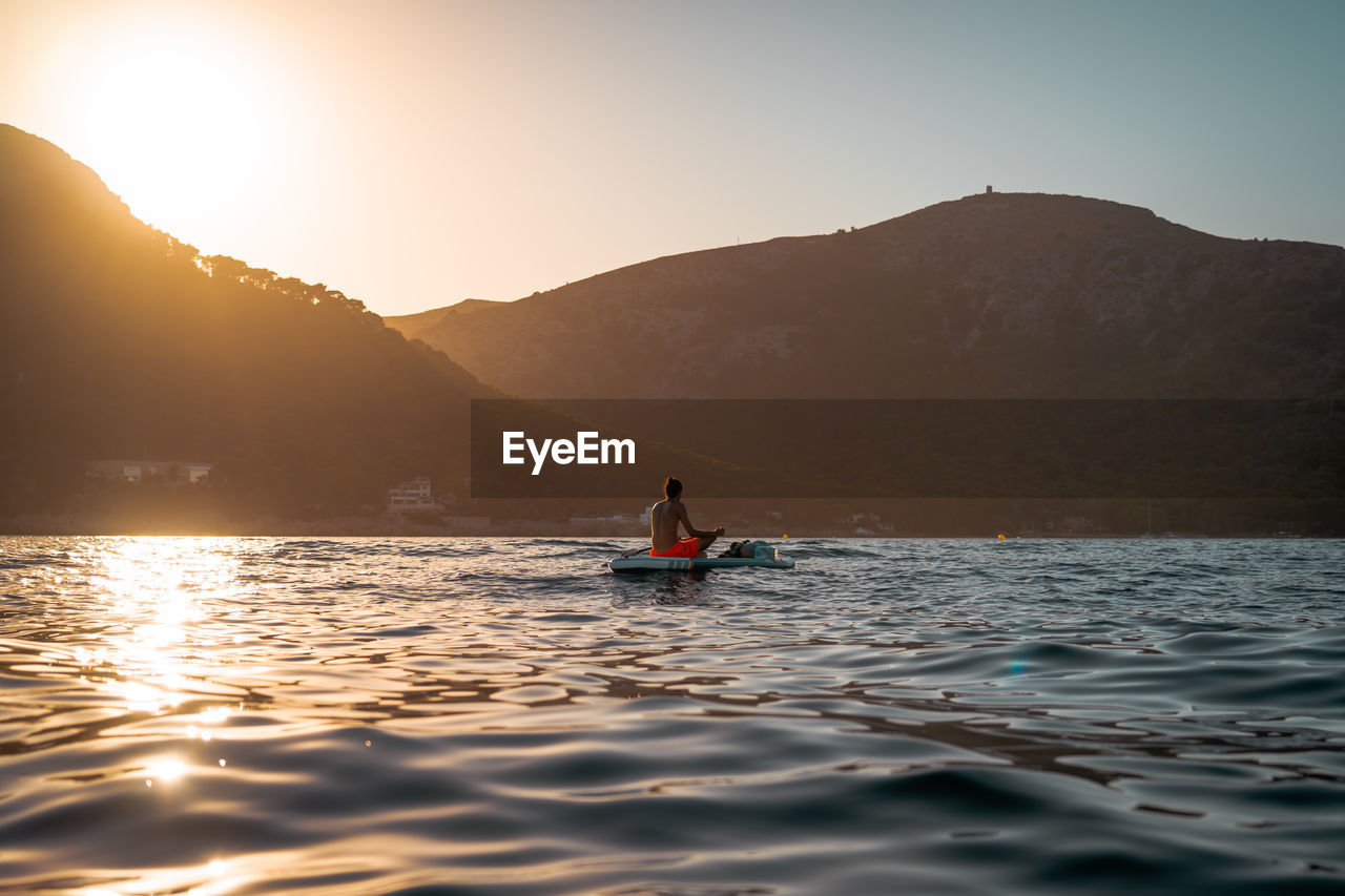Man sitting on boat in lake against sky during sunset