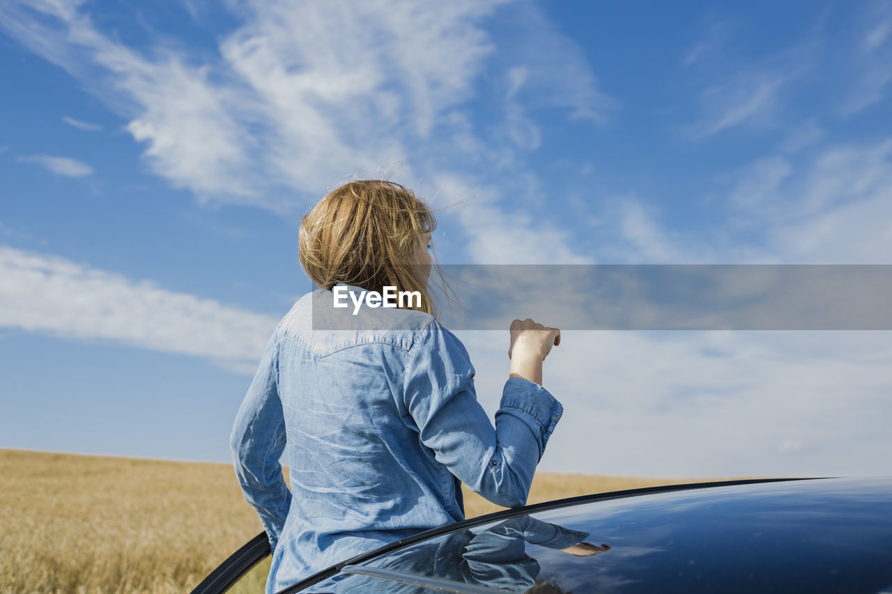 Woman peeking from car against sky