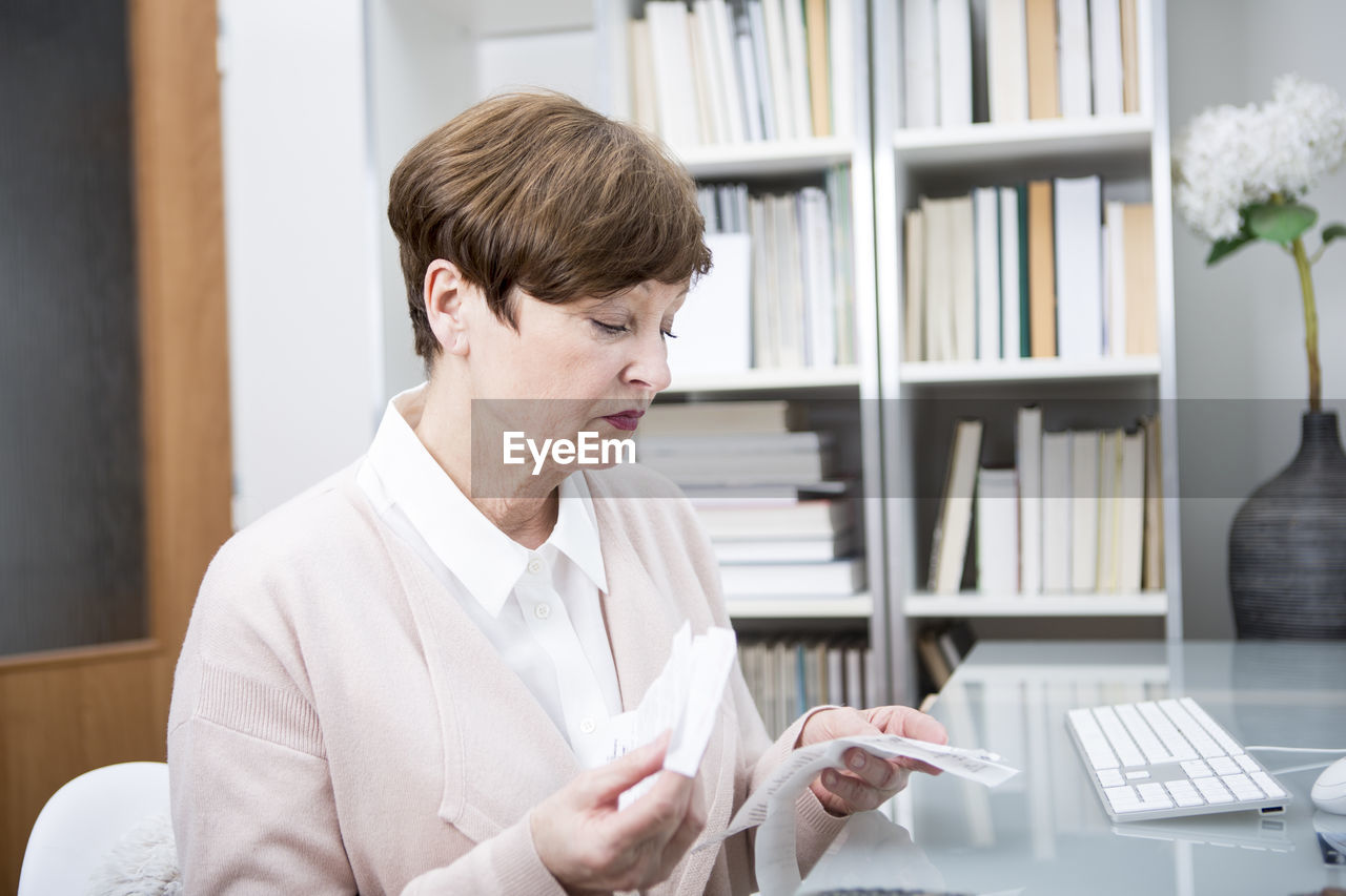 Senior woman sitting at table, checking bills