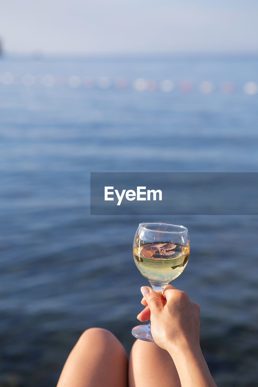 A girl holds in her hand a glass of white wine against the backdrop of a beautiful blue sea.