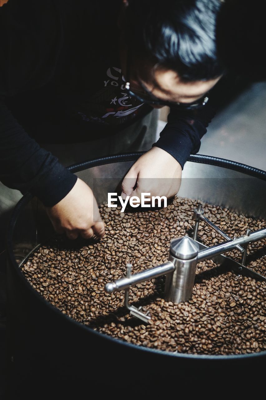 High angle view of man picking roasted coffee beans from container