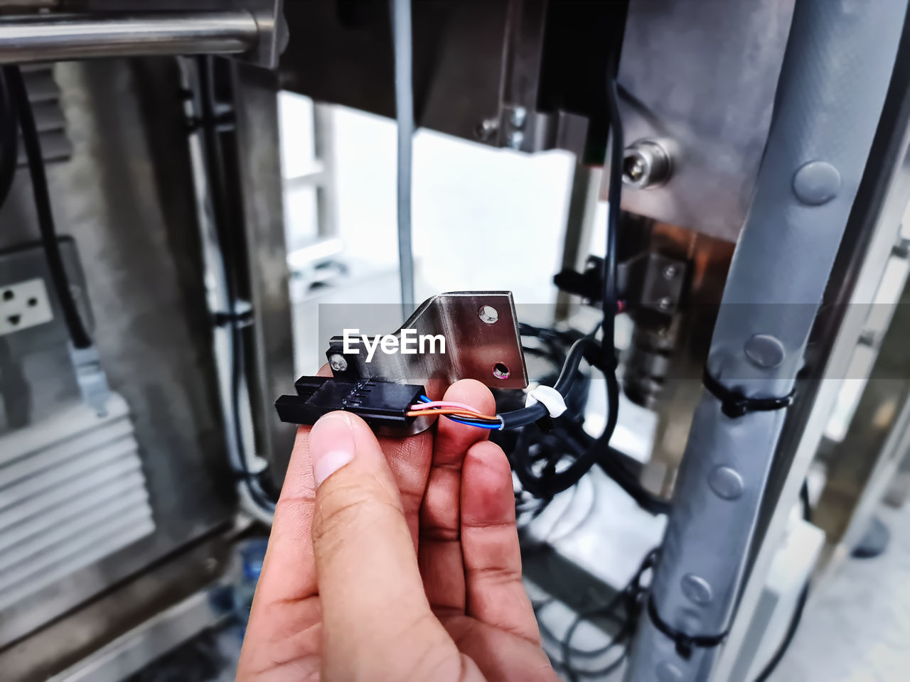 Hand holding stainless steel bracket and wired sensor for automated machine