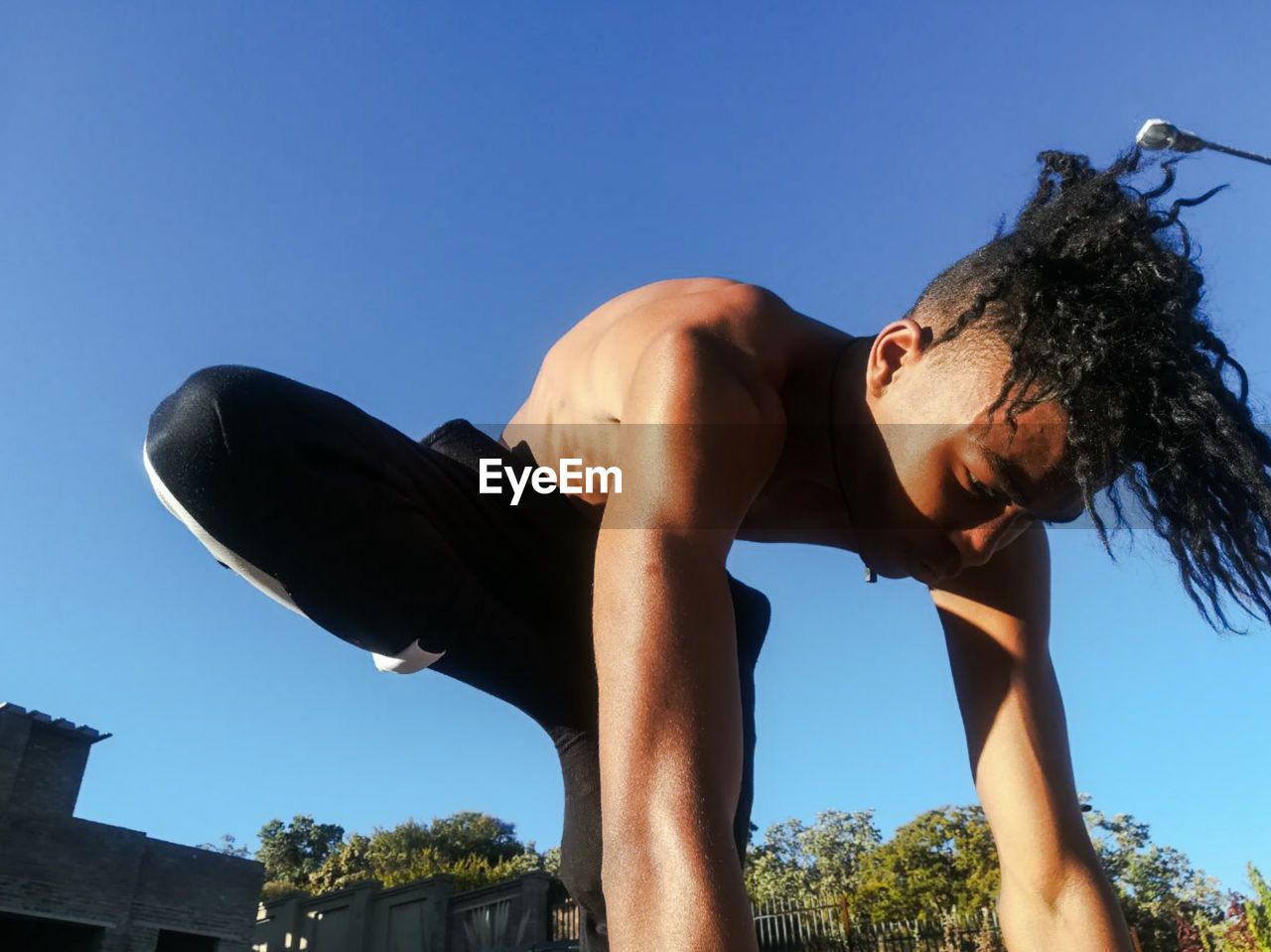 Low angle view of man exercising against blue sky during sunny day