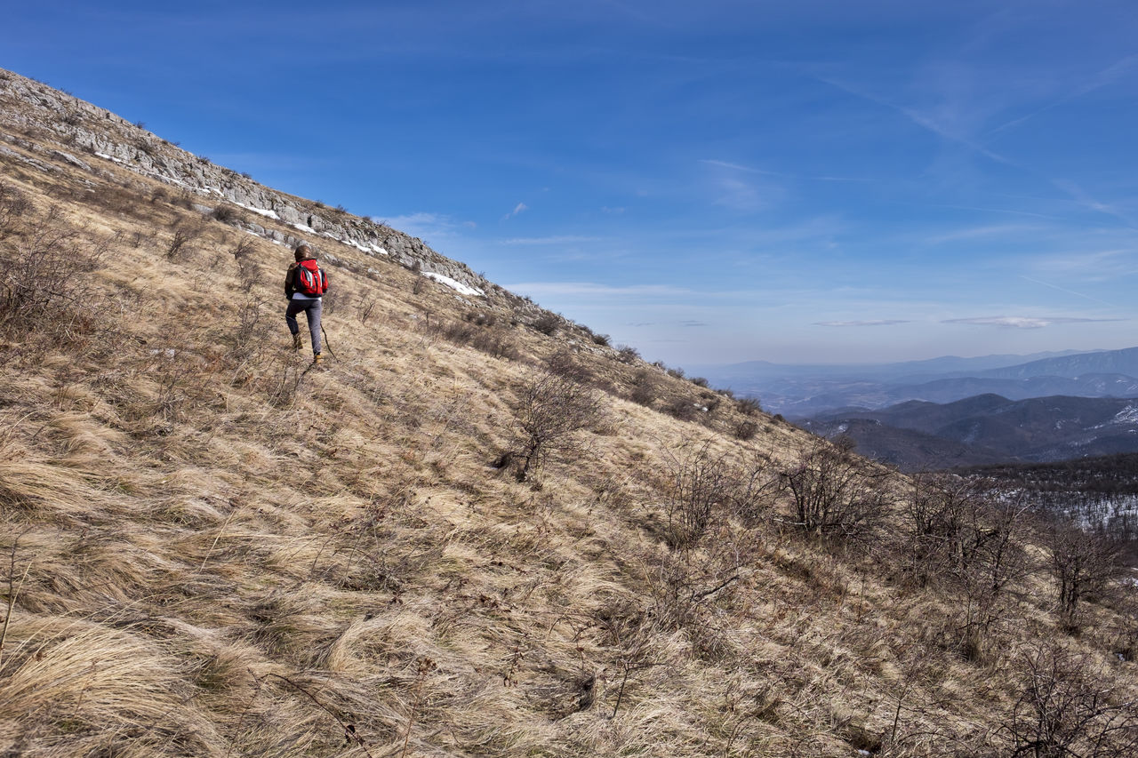 Rear view of male hiker with backpack walking on mountain against sky during sunny day