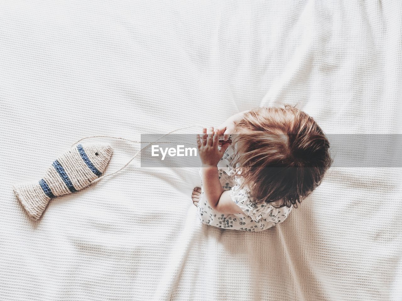 High angle view of baby toddler girl on bed with fish playing 