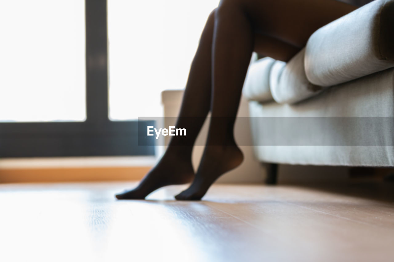 indoors, one person, adult, women, human leg, low section, flooring, sitting, limb, domestic room, home interior, lifestyles, young adult, barefoot, human limb, furniture, relaxation, shoe, living room, human foot, clothing, hardwood floor, domestic life, side view, high heels, female, wood, day, sofa, window