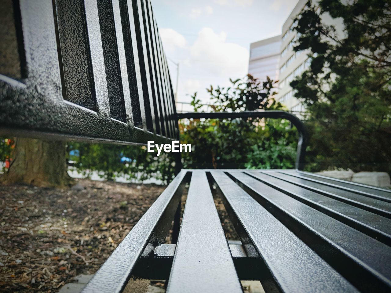 Close-up of bench in park by city against sky