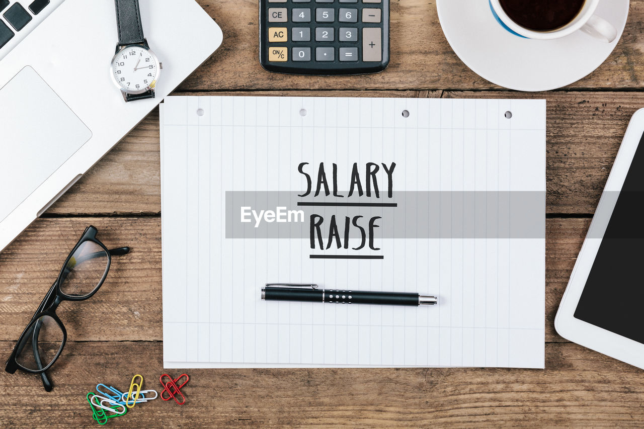 Salary raise written in notepad on office desk with electronic devices, computer and paper,